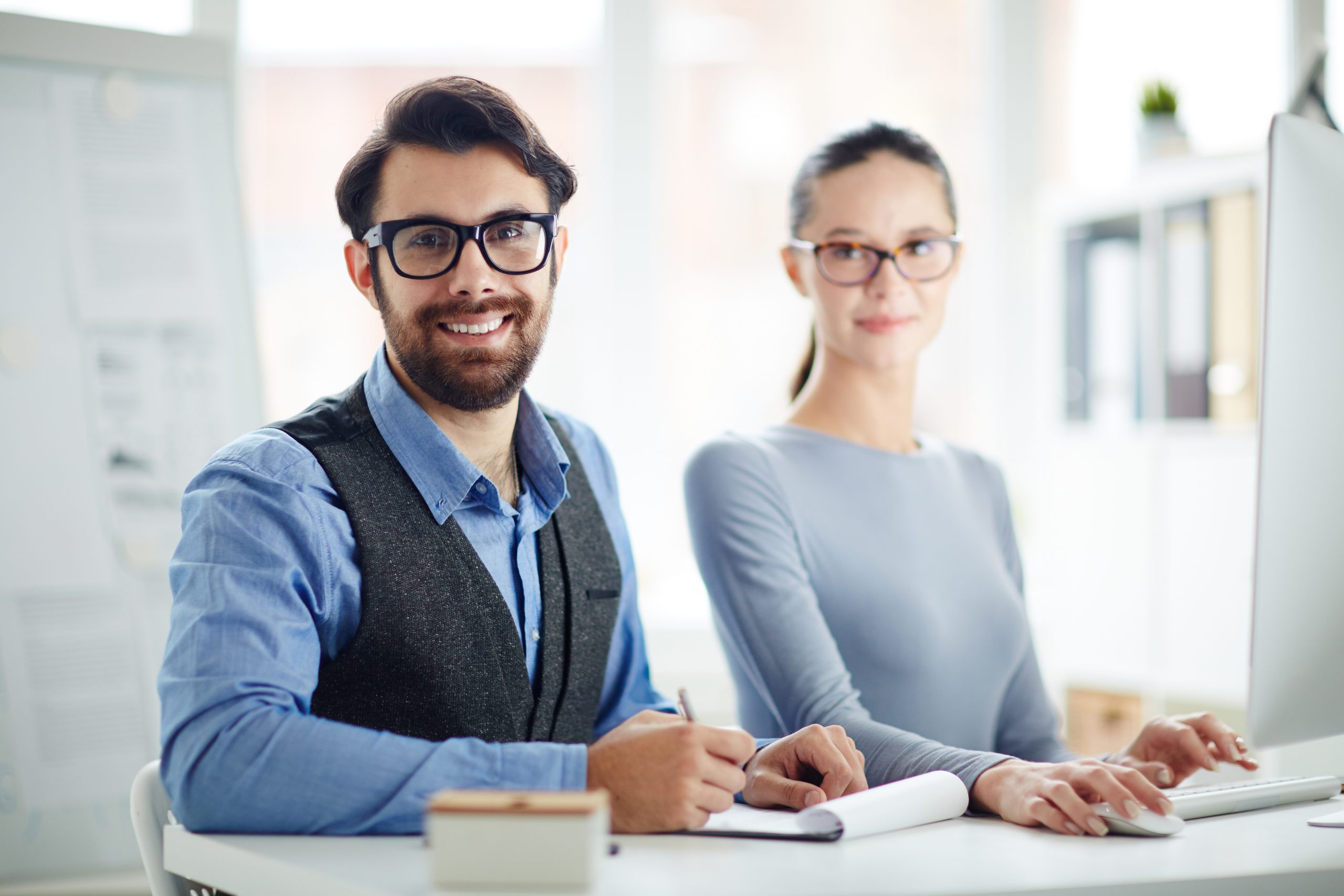Happy young colleagues looking at camera while organizing work in office